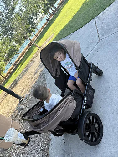 Two boys riding together in their brown Waggle wagon on a park path