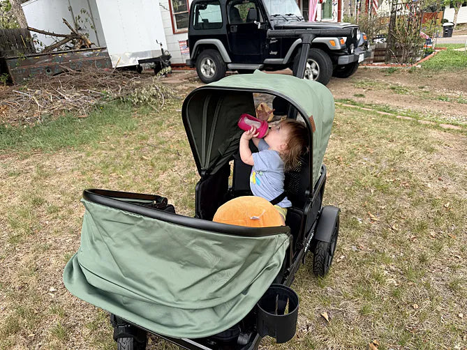 Toddler drinking from a pink cup while sitting in a green Waggle wagon