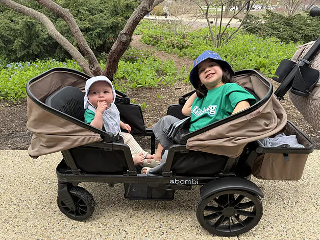 Two children smiling together in a brown Waggle wagon at a garden