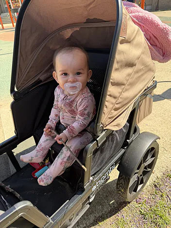 Baby sitting beneath a brown Waggle canopy at a sunny playground