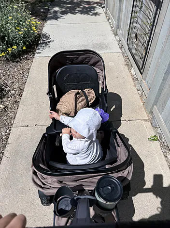 Toddler riding in a brown Waggle wagon along a sunny sidewalk