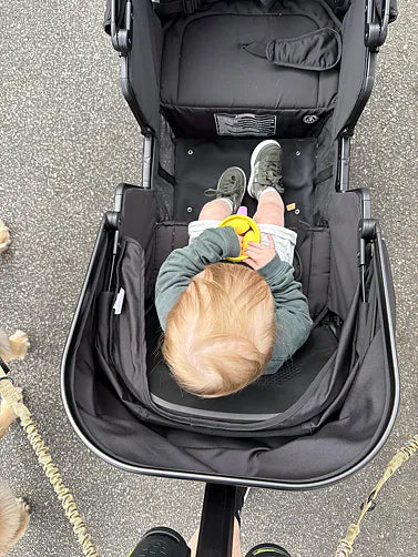 Toddler sitting in a black Waggle wagon and holding a yellow toy