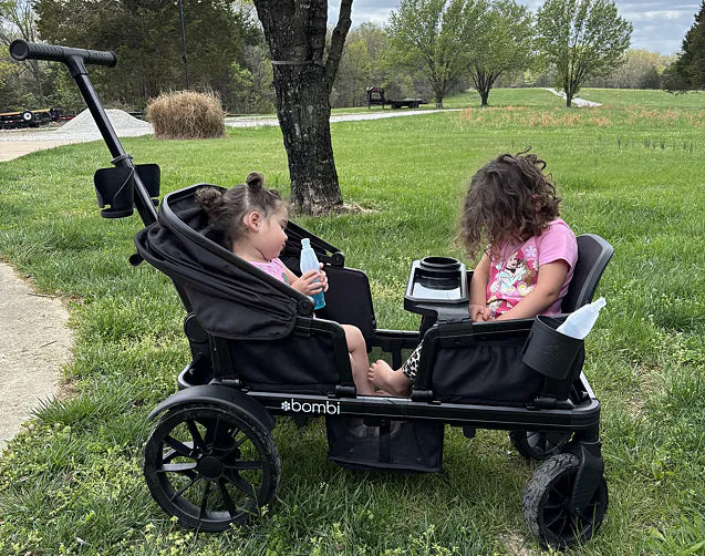 Two young girls sitting across from each other in a black Waggle wagon on grass